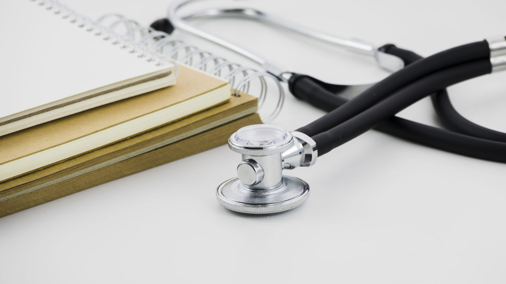 pilha-de-bloco-de-notas-em-espiral-e-estetoscopio-no-pano-de-fundo-branco